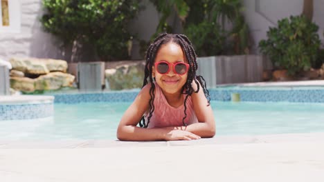 African-american-girl-wearing-sunglasses-in-swimming-pool-smiling-at-camera