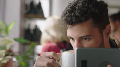 portrait attractive hispanic man using digital tablet computer in cafe drinking coffee browsing online reading social media messages on mobile device enjoying watching entertainment