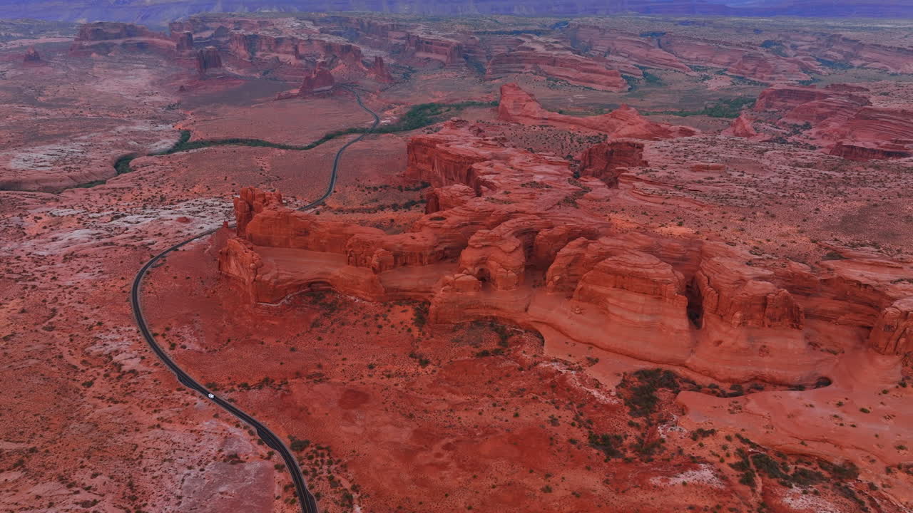 Bobil reiser langs motorveien og krysser det øde landskapet langs de røde steinene. Luftfoto av Arches nasjonalpark i Utah, USA ved solnedgang