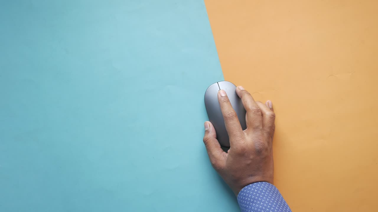 mano sosteniendo un ratón de computadora en un fondo de dos colores