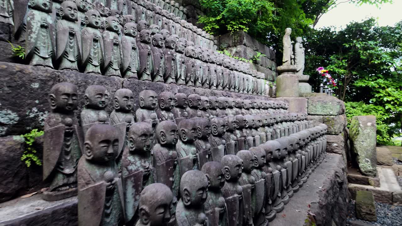 wide to close-up shot of stone Jizo statues at Hasedera Temple in Kamakura, Japan, surrounded by mossy stone steps and green foliage