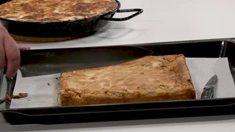 a baker skillfully slices into a freshly baked dessert on a baking tray. the cake appears golden brown and fluffy, ready to be served. delicious aromas fill the air, tempting everyone nearby