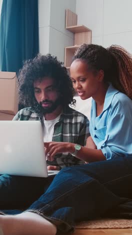 young successful family man and woman sit on floor after moving and use laptop