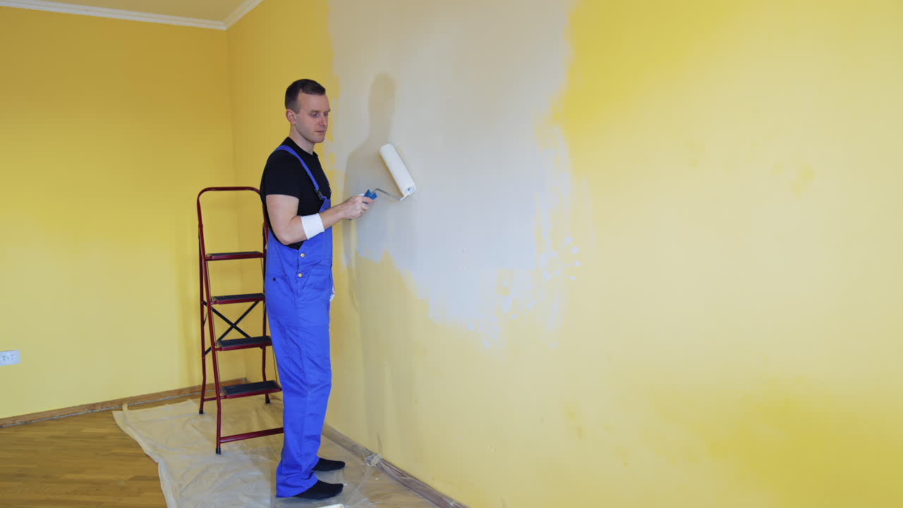 Handsome man with painting roller doing new indoor improvement. Professional builder renovating house.