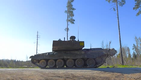 low angle footage of a challenger 2 4034 british military or army tank standing still on a gravel road in the middle of a green grassy field while it is moving its large cannon to search for enemies.