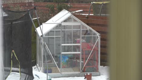 small glass greenhouse in garden during snowfall