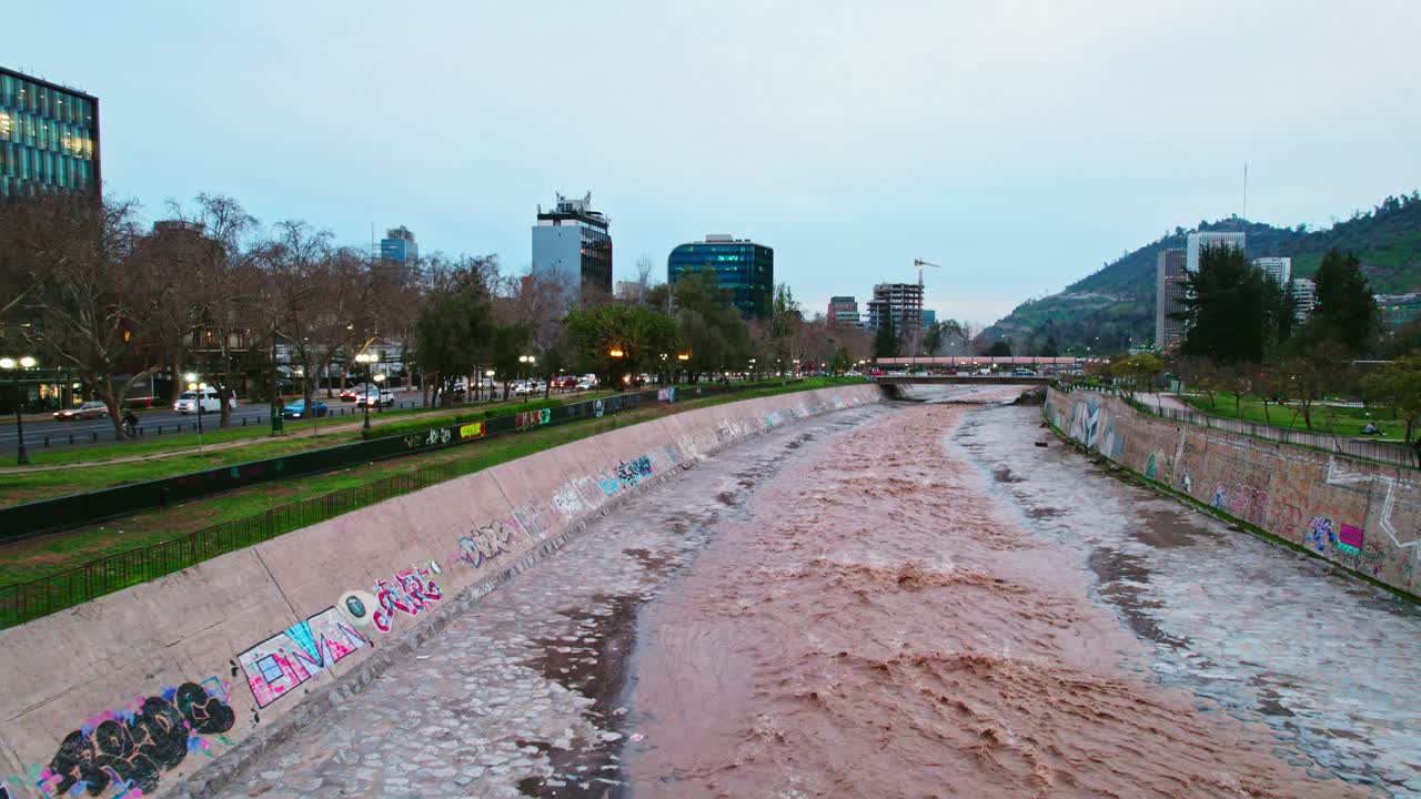 drone dolly en la toma del río mapocho agua que fluye a través de santiago chile con gran fuerza en una puesta de sol nublada