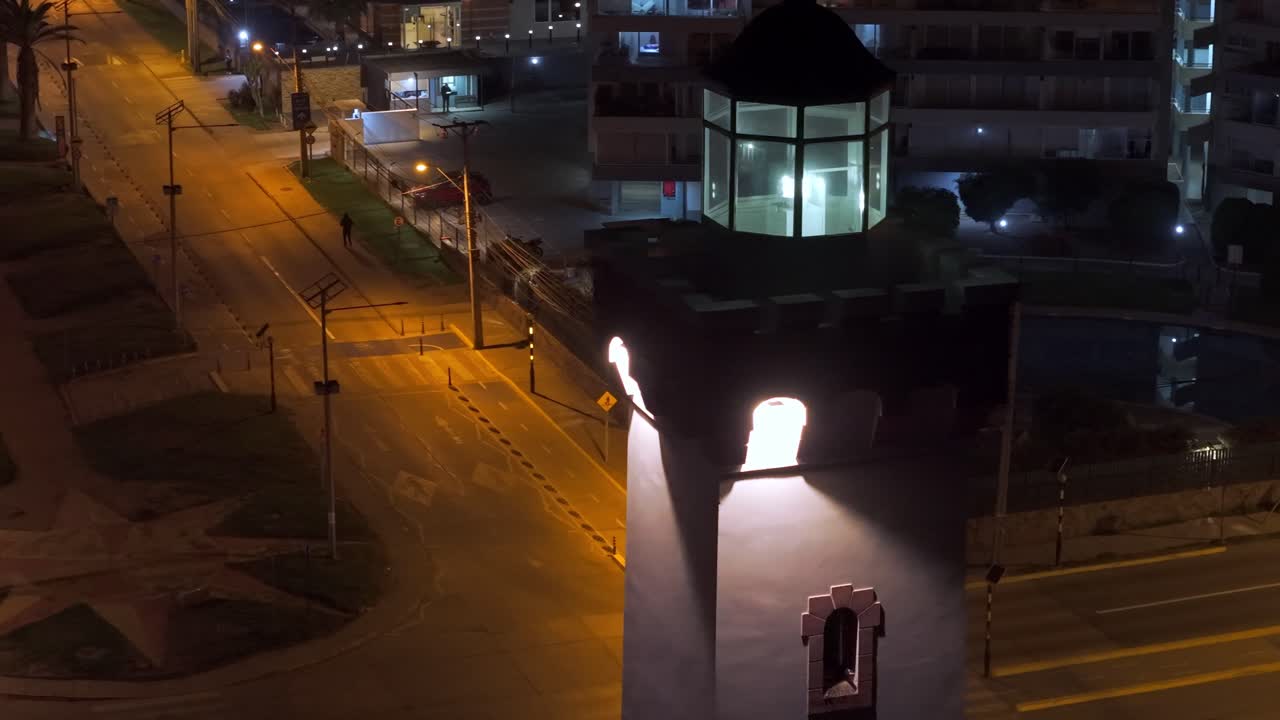 Night view of Faro de La Serena lighthouse glowing among urban streets and evening lights