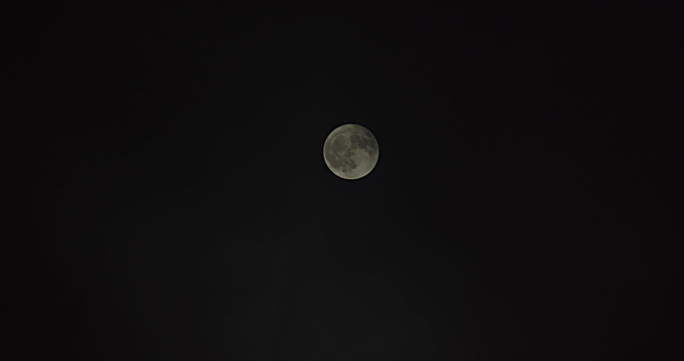 Plano geral da lua cheia sendo lentamente coberta por névoa passageira.