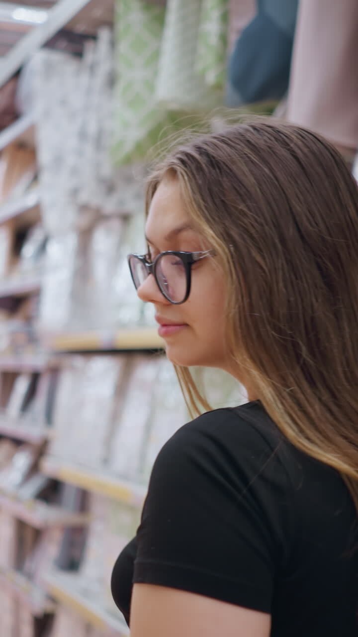 Cliente donna che cammina nel corridoio di un centro commerciale, mentre guarda i prodotti ben disposti sugli scaffali. Indossa un abbigliamento casual con jeans e top nero e porta delle borse della spesa in un ambiente commerciale ben illuminato