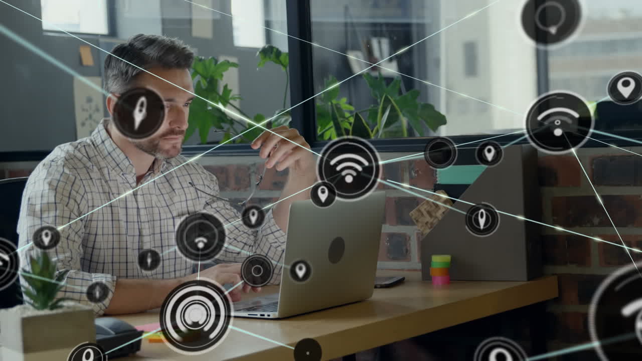 animación de una red de iconos digitales contra un hombre caucásico que usa una computadora portátil en la oficina