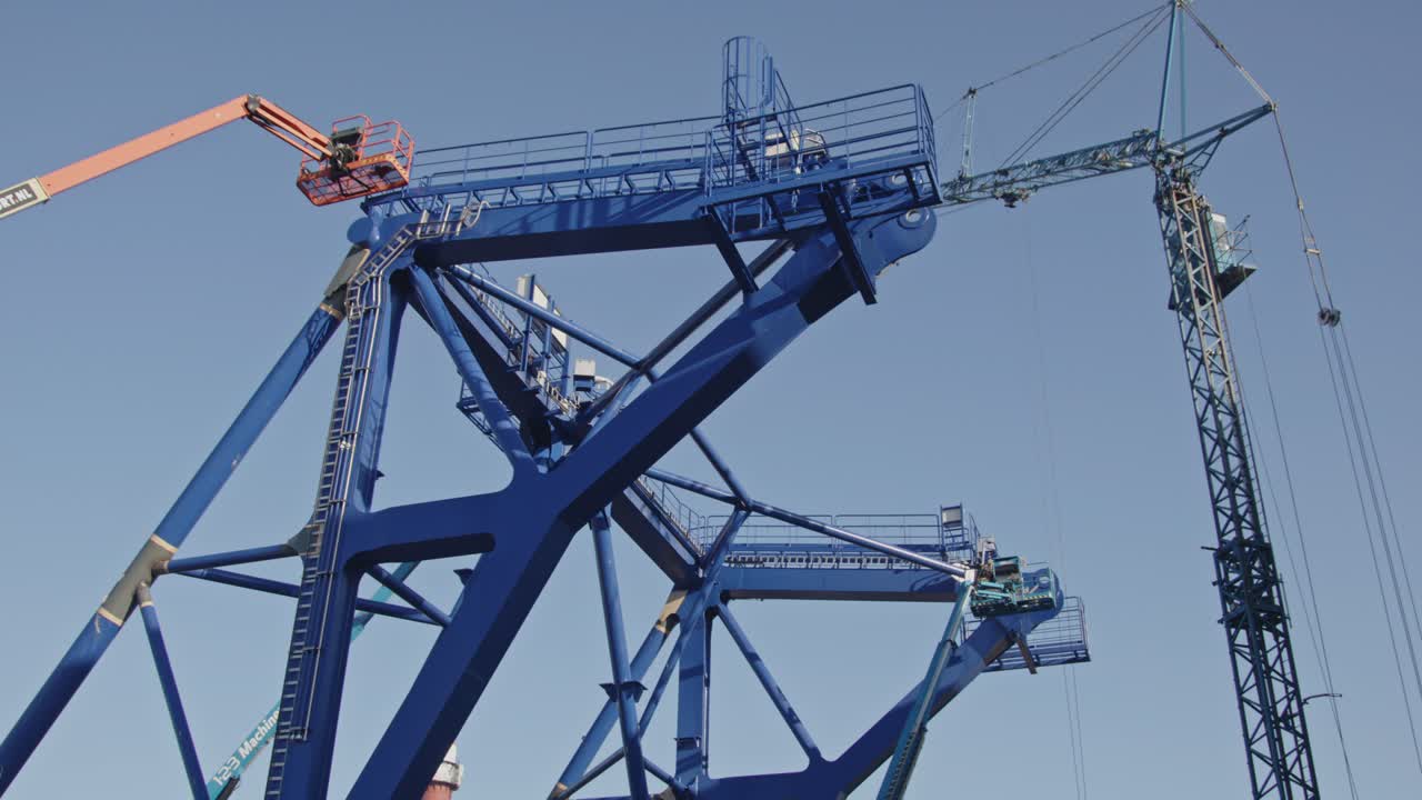 Low angle pan of a pre-piling template being constructed at a dock in a harbor. The piling template will be used to place offshore wind turbines in deep water