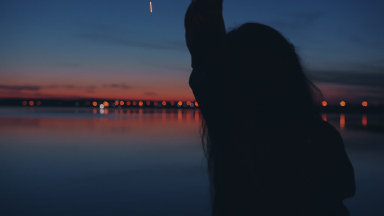 Girl with sparklers at sunset by the lake