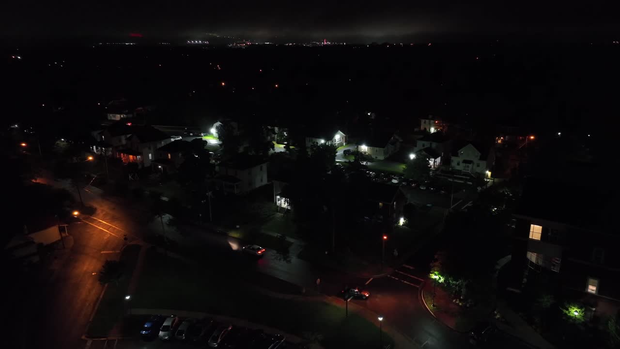Driving cars on main street of small town at night. American housing area with warm lighting streetlights. Aerial top down tracking shot. Virginia, USA.