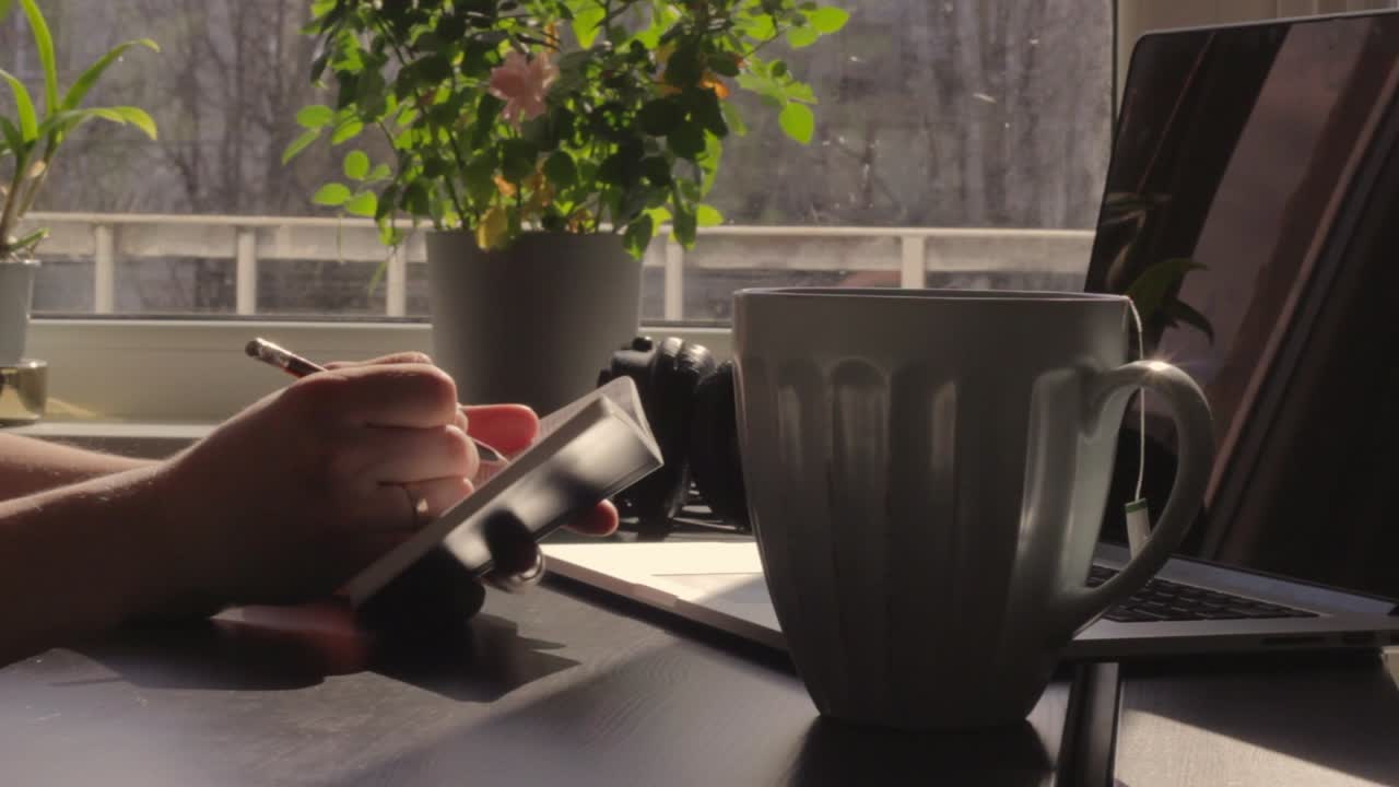 Lista delle cose da fare al mattino, primo piano di mani che spuntano le voci, scrivania con laptop da lavoro, giorno