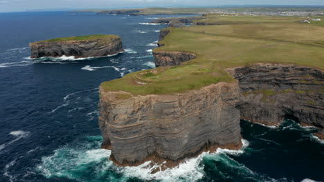 Aerial-descending-footage-of-high-rocky-cliffs-on-sea-coast.-Waves-crashing-on-rock-and-splashing.-Beautiful-panoramic-natural-scenery.-Kilkee-Cliff-Walk,-Ireland
