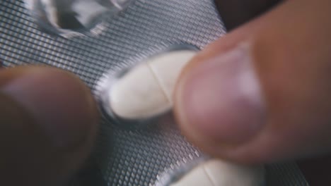 man holds blister with white pills on light background