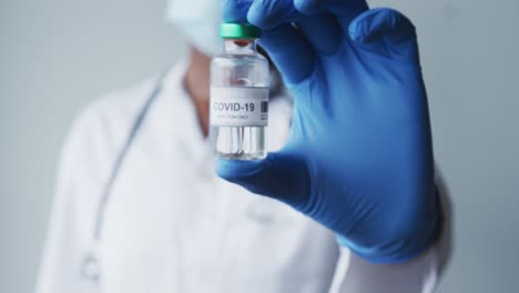 caucasian male doctor wearing protective gloves holding covid-19 vaccine