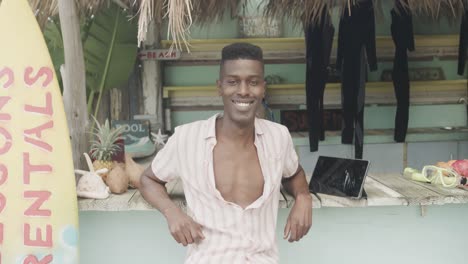 retrato de un feliz hombre afroamericano inclinado y sonriendo en una cabaña de alquiler de tablas de surf, en cámara lenta.