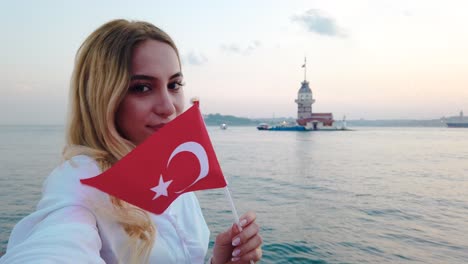 slow motion: attractive beautiful girl waves turkish flag and enjoys sunset view of bosphorus and maiden tower in istanbul,turkey