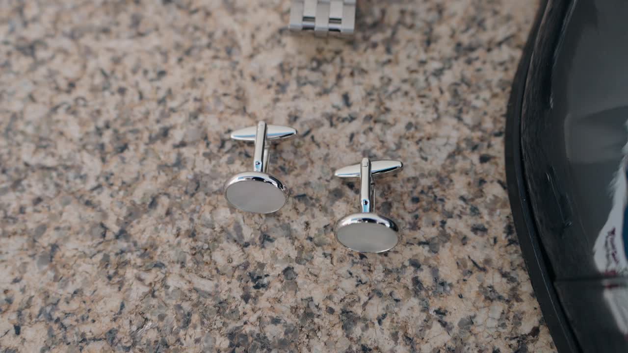 close up of round silver cufflinks on granite beside a polished black leather shoe