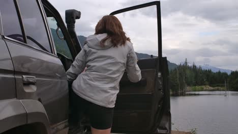young female gets out landcruiser jeep and looks at forest lake slomo