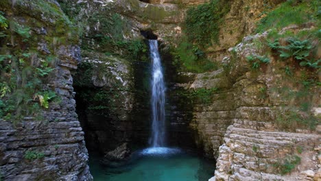 Cascada-En-La-Ladera-De-Una-Montaña-Rocosa-Que-Fluye-Agua-Limpia-Dentro-Del-Estanque-Esmeralda-En-Albania