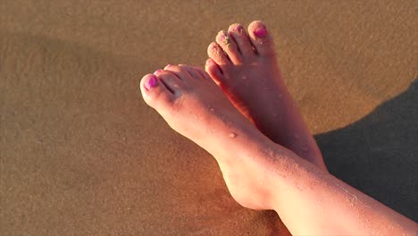 le gambe di una ragazza su una spiaggia sabbiosa con le onde che si infrangono sulle sue gambe