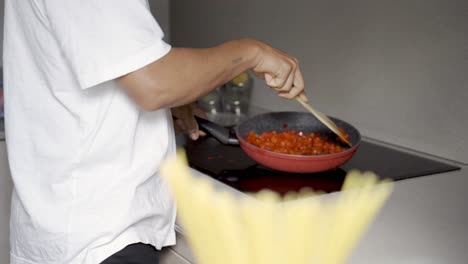 hombre étnico anónimo freyendo tomates en la sartén en la cocina