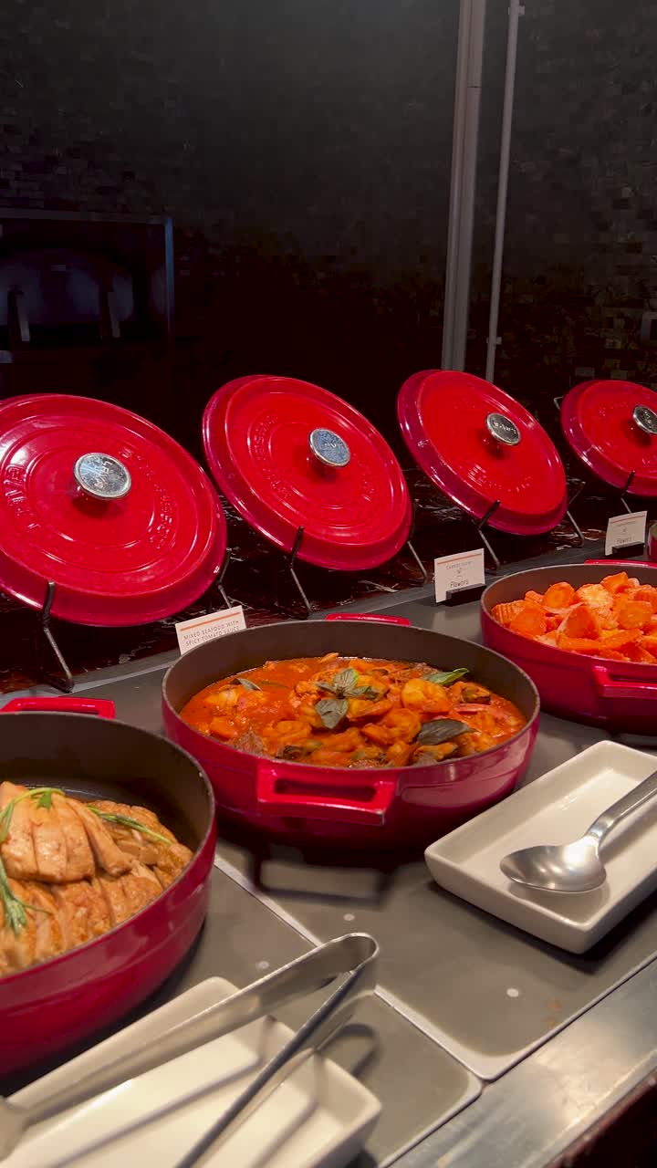 La telecamera effettua una panoramica su un buffet professionale con pentole in ghisa rosse piene di cibo.