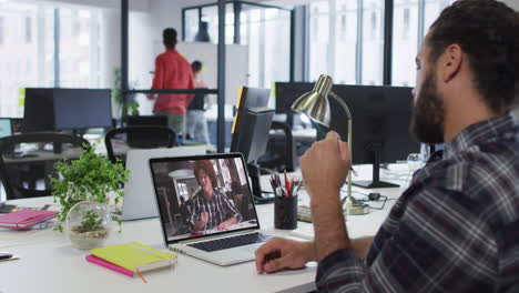 middle eastern man talking on video call with male office colleague on laptop at office
