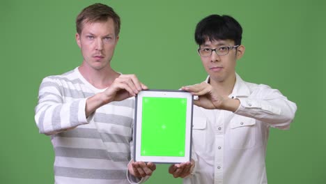 two young multi-ethnic businessmen showing digital tablet to the camera together