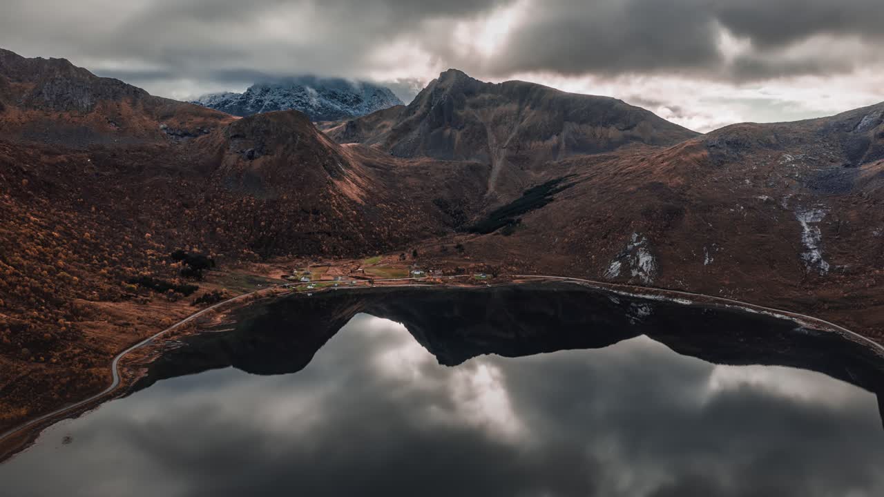 Towering mountains and grey clouds reflected in the calm mirrorlike waters of the fjord