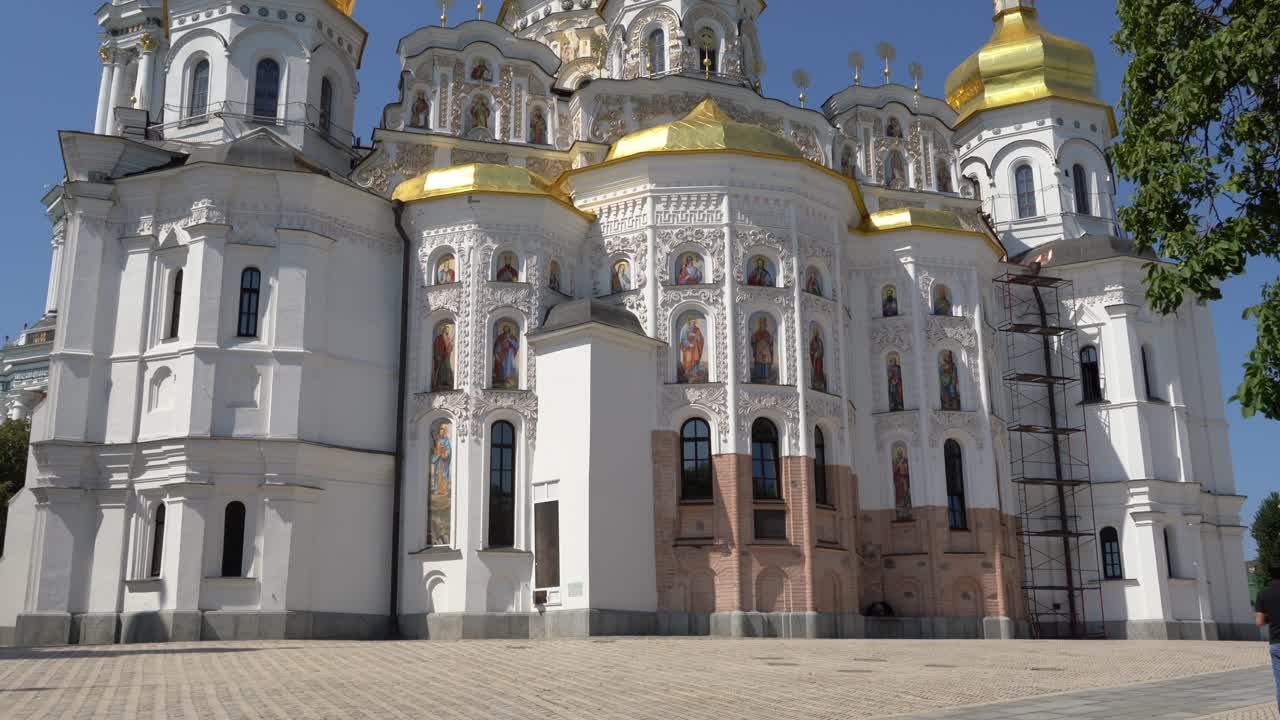 Ukraine,Kyiv,Pechersk Lavra, close up of Lavra's main building, camera tilts up from bottom up, towers and golden domes on a sunny day. Sun shines on the golden domes with blue skies at the back.