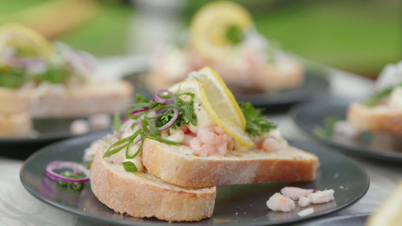 mano de una mujer exprimiendo un limón sobre sándwiches tradicionales de camarones daneses en platos - cámara lenta