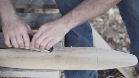 Man planes a wooden canoe paddle