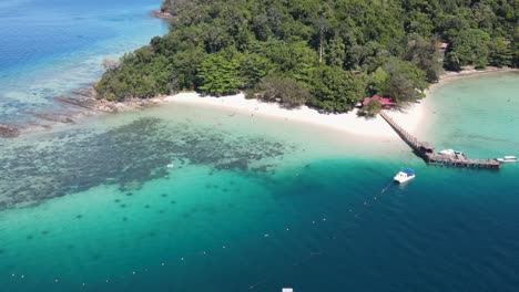 Aerial-View-Of-Sapi-Island-Beach-Coastline-On-Clear-Sunny-Day-With-Pier-and-Resort-Buildings