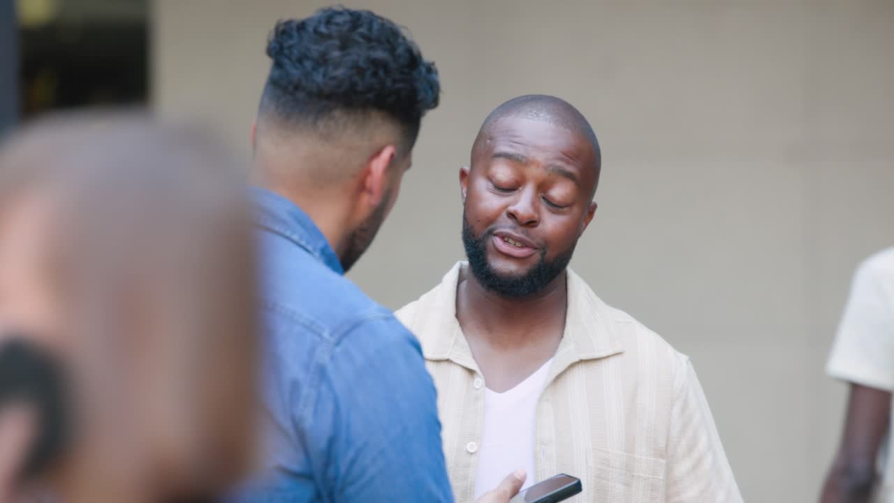 Beige-overshirt man is reading phone shown by blue-shirt man to check text at entrance, smiling