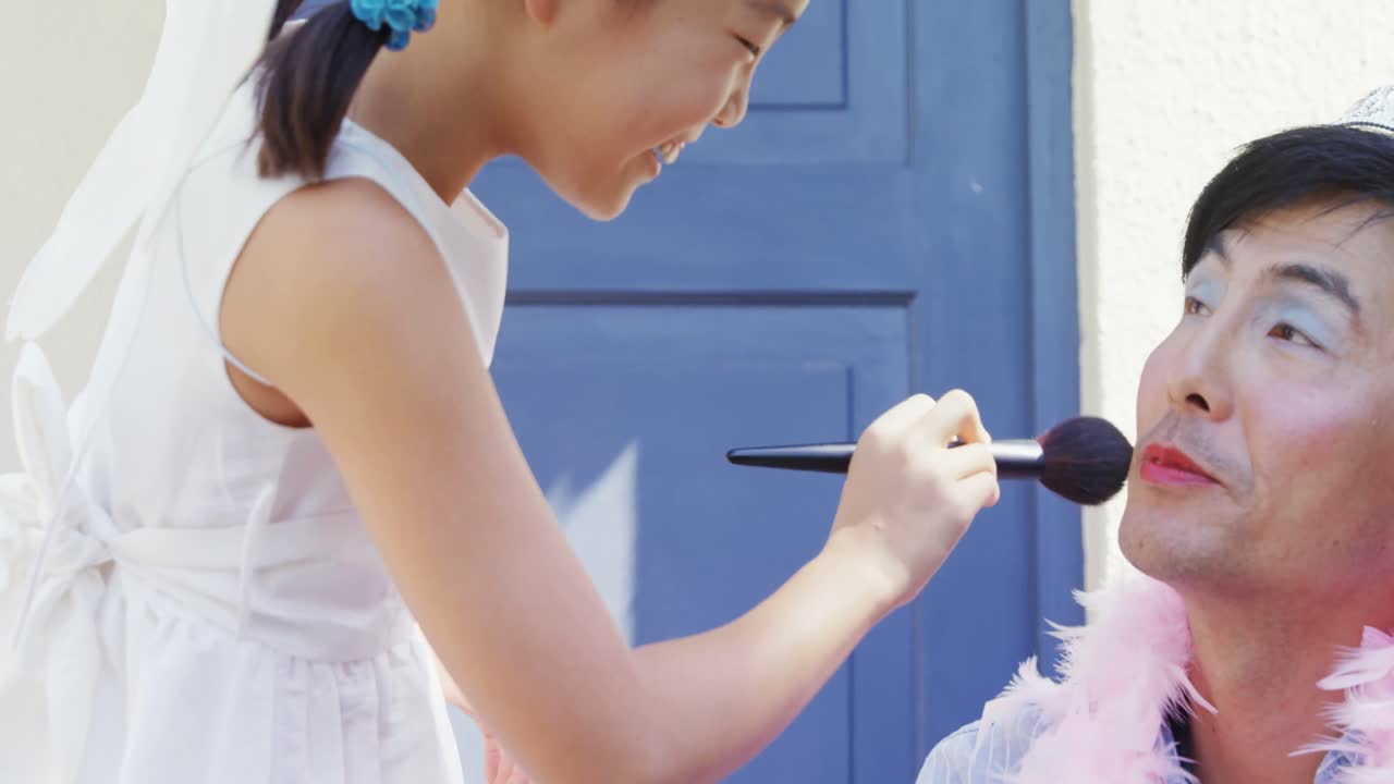 요정 의상 을 입은 귀여운 딸 이 아버지 의 얼굴 에 메이크업 을 하고 있다