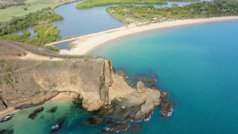 drone view of a blue lagoon with a cliff, a beach and water streams in a tropical area during the day