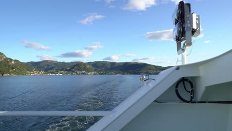 passengers view from hydrogen powered ferry hydra - walking against fence and looking astern with hjelmeland in background - ferry crossing to nesvik during sunny summer day - norway