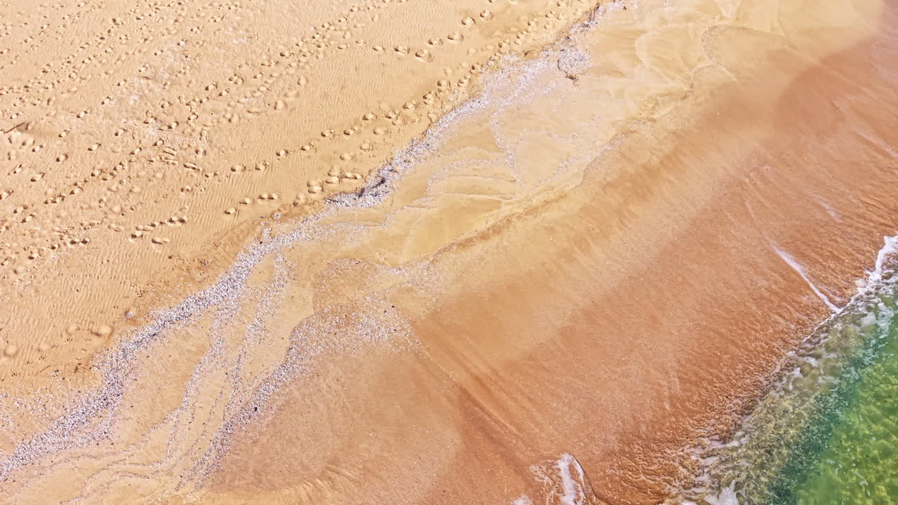 Gentle waves caress the golden sand under a warm sun at the shoreline, inviting tranquility and serene moments along the coast