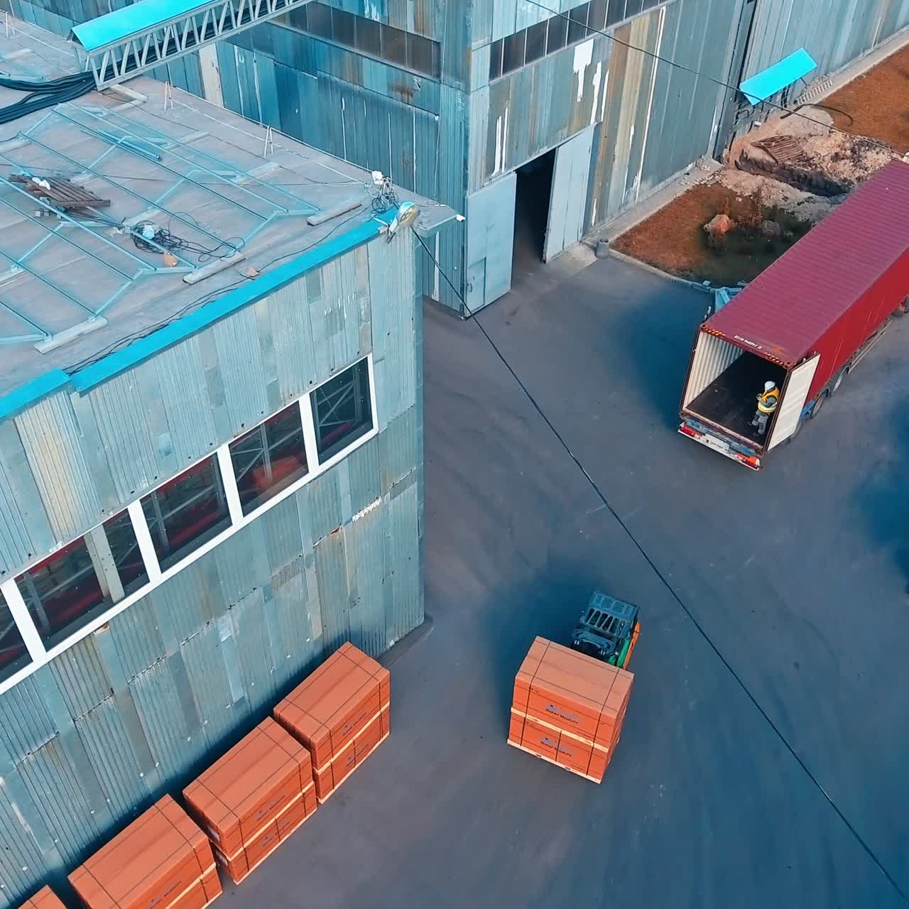 Unloading the long lorry with skid loader machine. Lots of empty barrels are near the car at the industrial area