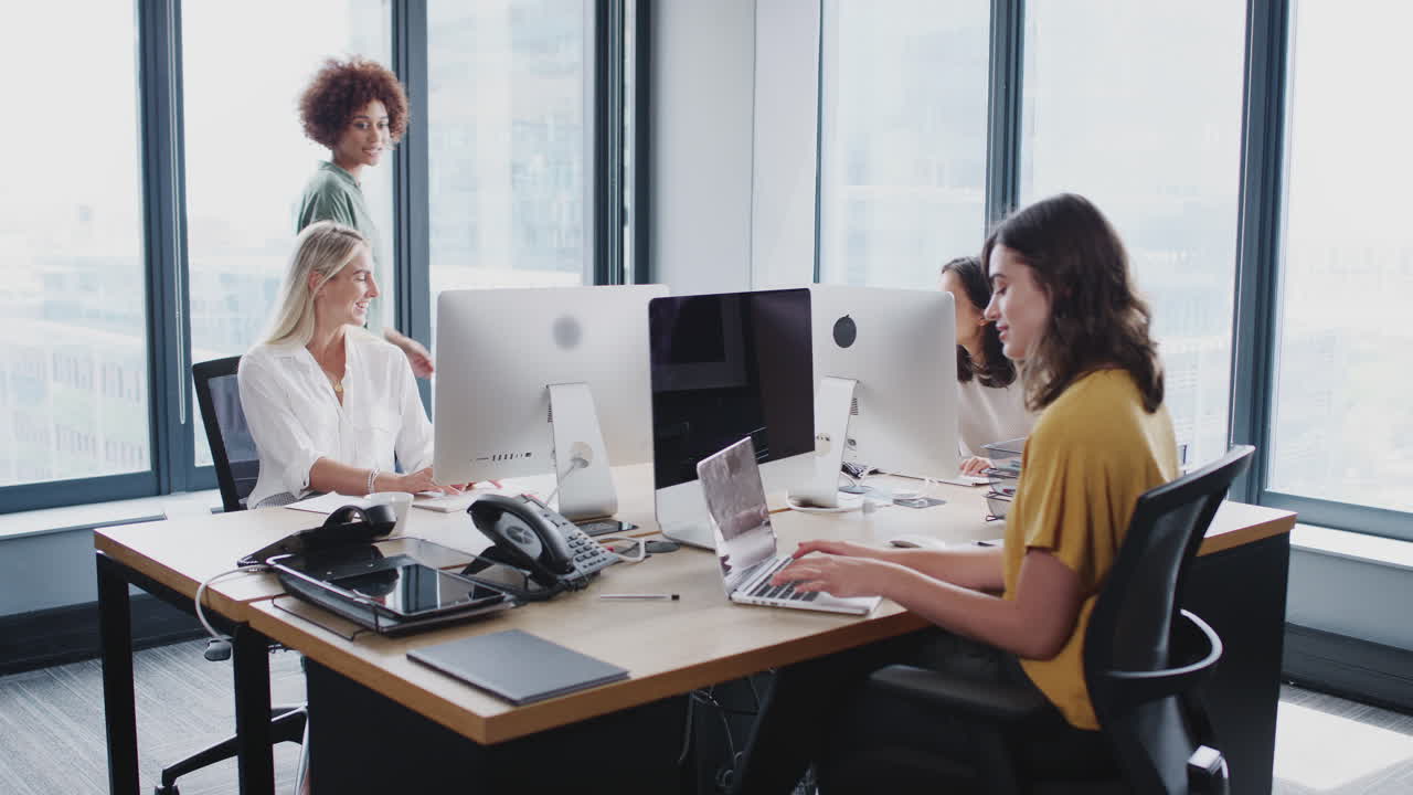 밀레니얼 흑인 여성이 사무실을 돌아다니며 여성 창의적인 동료들과 대화하고 있습니다.