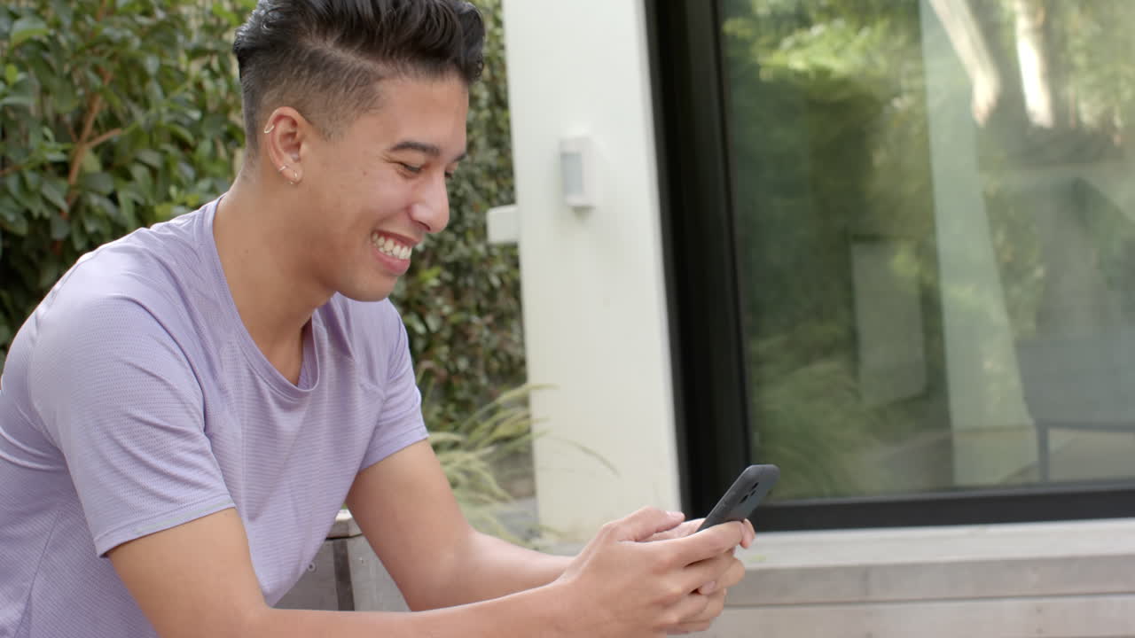 Laughing and texting, young man enjoying time on smartphone outdoors, copy space