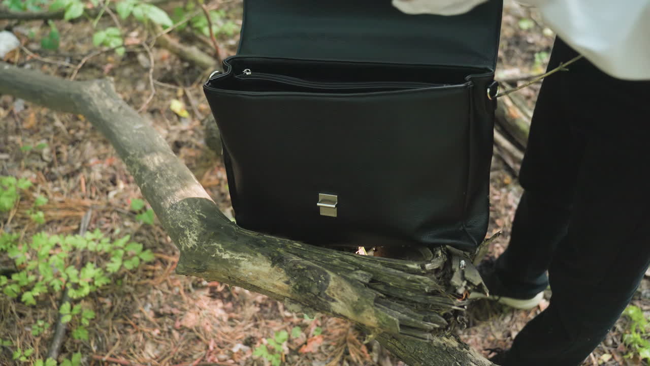Close-up view of botany student in white shirt handling black bag on fallen tree in forest, removing white coat while surrounded by greenery and natural sunlight creating woodland atmosphere