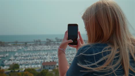 una adolescente rubia caucásica tomando fotografías con su teléfono celular de un puerto en california