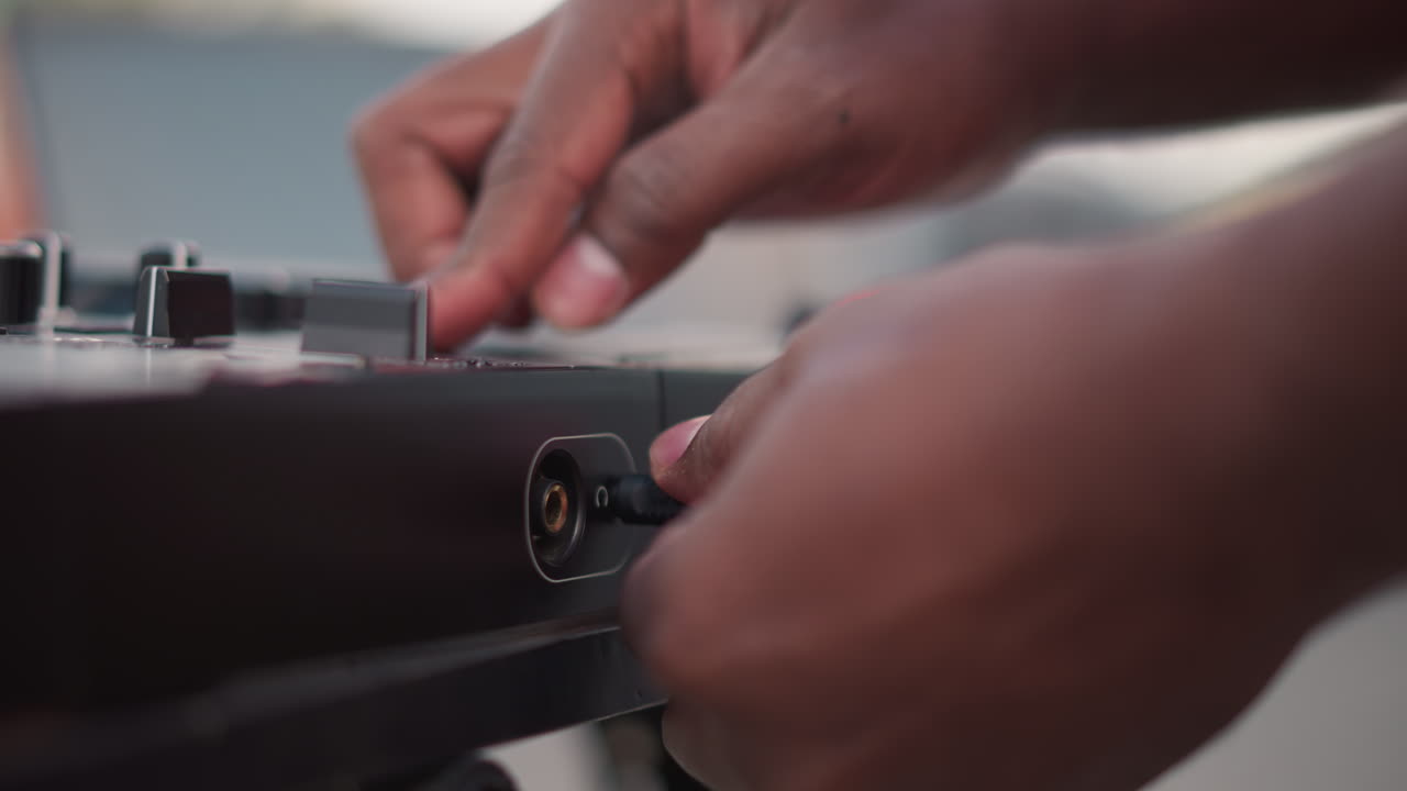 closeup hands adjusting mixer knobs and connecting cable dynamic street setup confident fingers tweak fader, seat connector, and test jack with shallow depth of field and warm evening tones scene