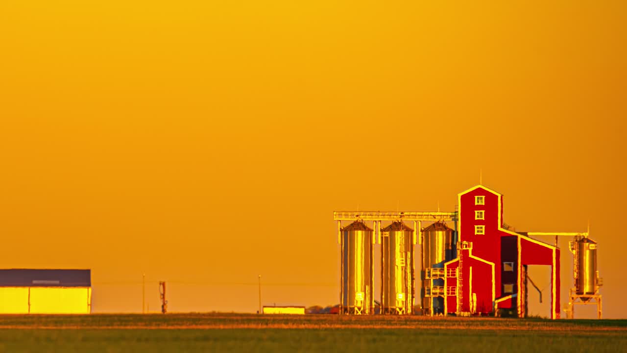 Ein leuchtend gelber Sonnenaufgang erhellt einen Bauernhof mit Silos.