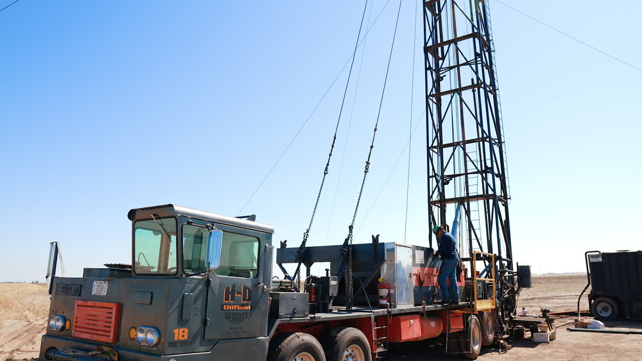Modern truck with a tower at the back. Worker wearing helmet stands at the deck. Low angle view at the drilling equipment.